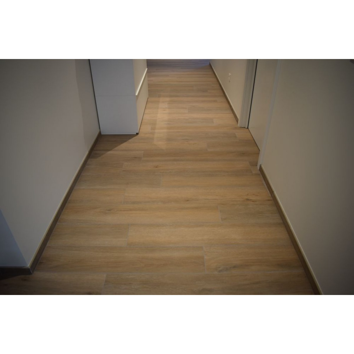 Carrelage aspect bois marron clair sans motifs taille 20x120 cm dans un couloir aux murs blancs et portes blanches