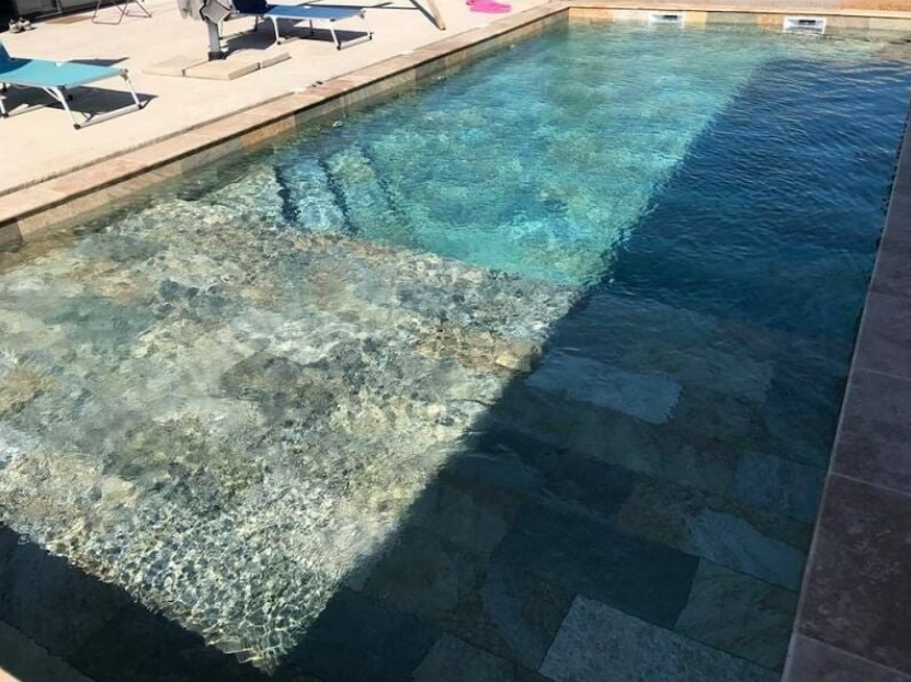 Carrelage effet pierre marron nuancé 30x60 cm dans une piscine extérieure à leau claire avec bordures et transats