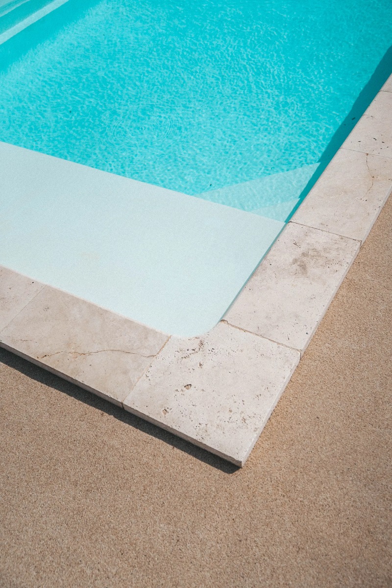 Carrelage effet pierre couleur beige sans motifs sur le bord dune piscine avec eau turquoise et revêtement sable