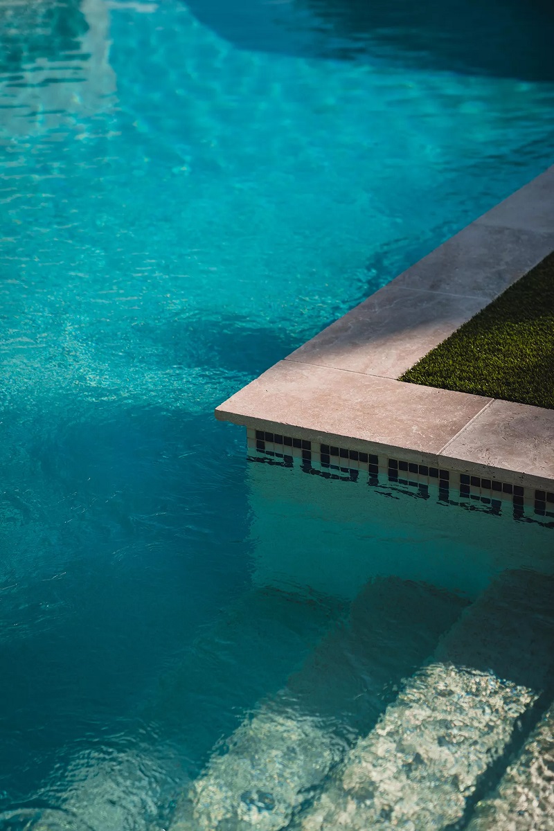 Carrelage effet pierre beige bord de piscine sur fond deau turquoise avec gazon artificiel et mosaïque décorative