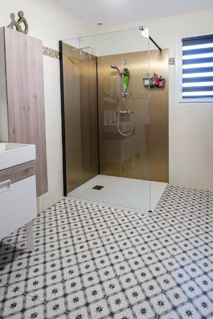 Carreau de ciment or avec motifs floraux 30x30 cm dans une salle de bain beige avec douche vitrée et meubles en bois