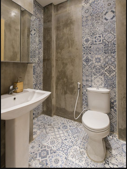 Carreau de ciment bleu aux motifs variés 45x45 cm dans une salle de bain aux murs gris béton avec WC et lavabo blancs