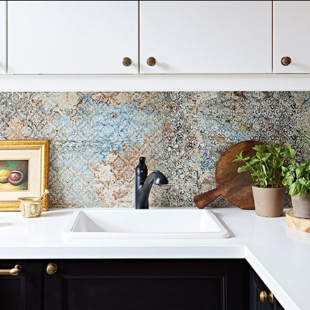 Carrelage effet tissu beige avec motifs multicolores 50x100 cm sur un mur de cuisine, meubles blancs et comptoir noir, touches de vert des plantes