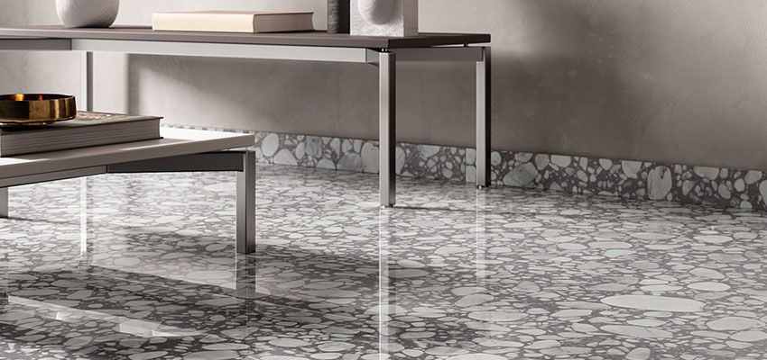 Carrelage Terrazzo gris avec éclats blancs 60x60 cm dans un salon moderne aux murs gris et une table en verre et métal