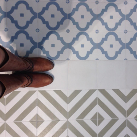 Carreau de ciment beige avec motifs géométriques bleus et blancs 20x20 cm sur un sol de pièce neutre avec pieds en bottines brunes