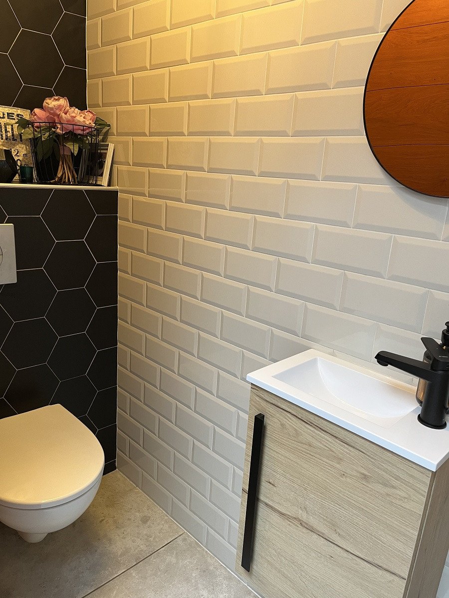 Carrelage uni noir et crème sans motifs dans une salle de bain avec meuble bois et vase fleurs roses sur fond gris