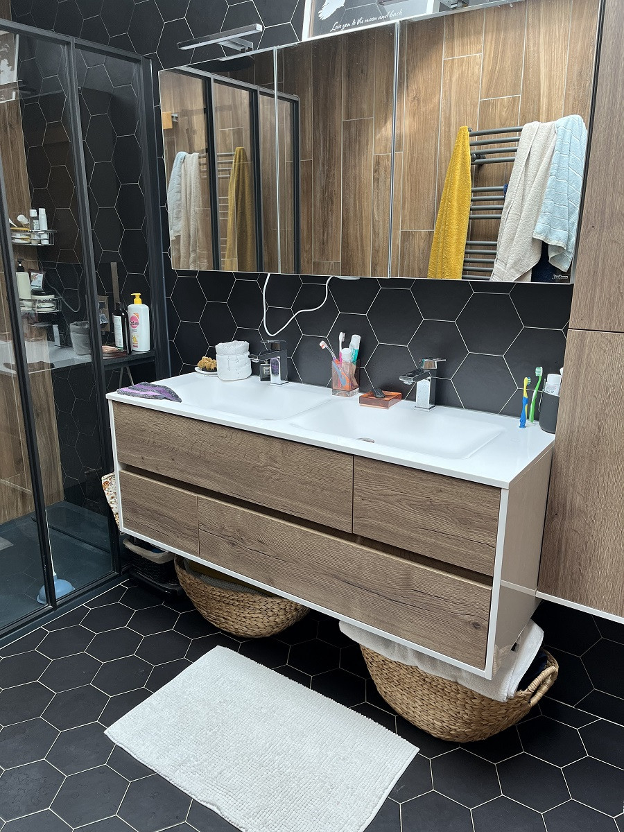 Carrelage uni noir sans motif dans une salle de bain moderne meubles en bois miroir serviettes jaune et bleue tapis blanc