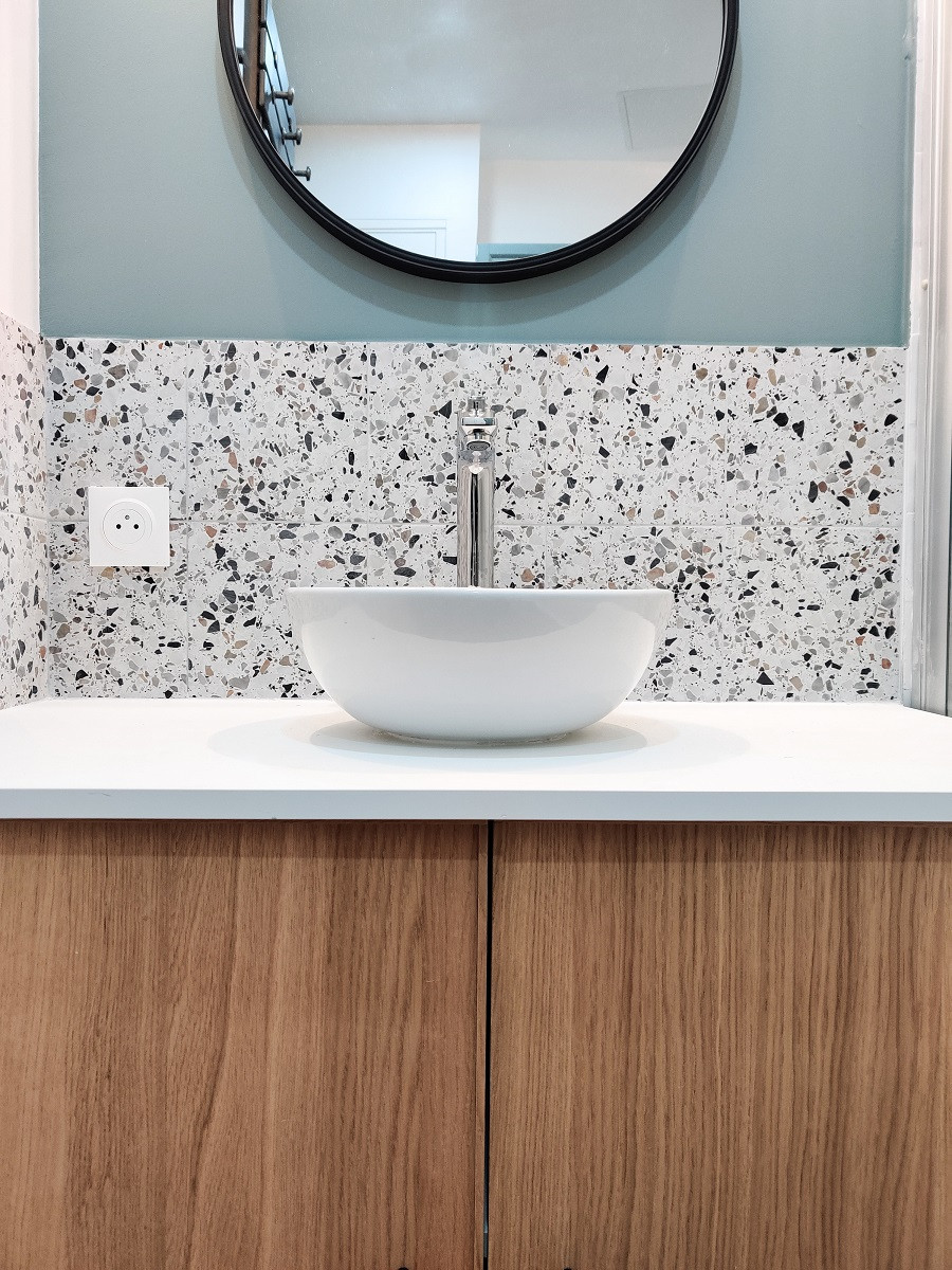 Carrelage Terrazzo blanc parsemé de gris et noir 20x20 cm dans salle de bain aux murs bleus avec vasque blanche et miroir rond