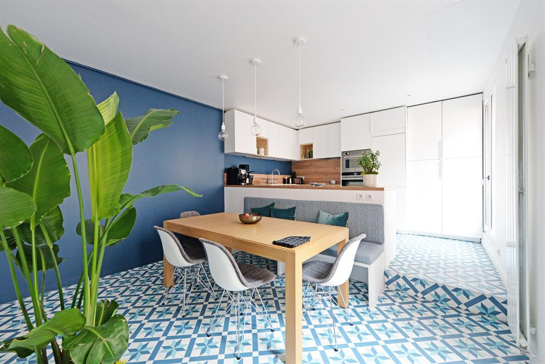 Carreau de ciment bleu et blanc géométrique 30x30 cm dans une cuisine moderne aux murs bleus et meubles blancs, avec table en bois et plantes vertes
