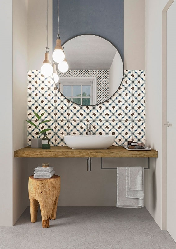 Carreau de ciment bleu avec motifs étoiles sur un mur de salle de bain beige avec miroir rond, vasque blanche et éclairage suspendu