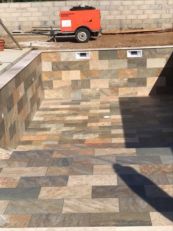 Carrelage aspect pierre nuances de beige sans motifs 30x60 cm dans piscine extérieure, murs gris, équipement de chantier en fond