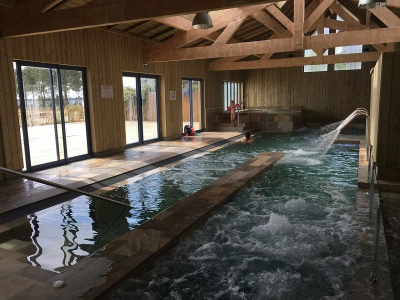 Carrelage aspect pierre beige sans motifs 30x60 cm dans une piscine intérieure avec murs en bois et enfants jouant