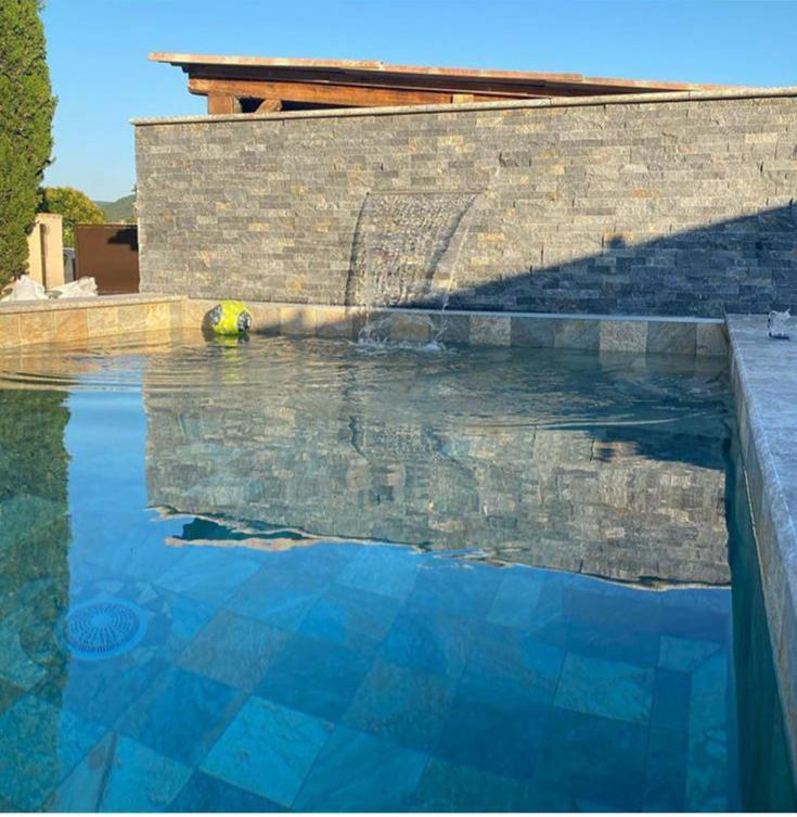Carrelage aspect pierre beige sans motifs 30x60 cm dans une piscine extérieure eau bleu ciel bordures et murs en pierres grises