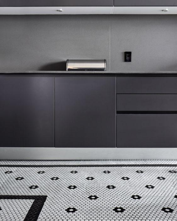 Carrelage noir uni et mosaïque motifs géométriques blanc dans une cuisine moderne avec meubles anthracite et plan de travail gris