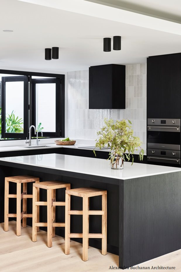 Carrelage Zellige Blanc brillant taille 6,5X20 sur un mur de cuisine moderne avec meubles noirs, plans de travail en quartz, tabourets en bois clair