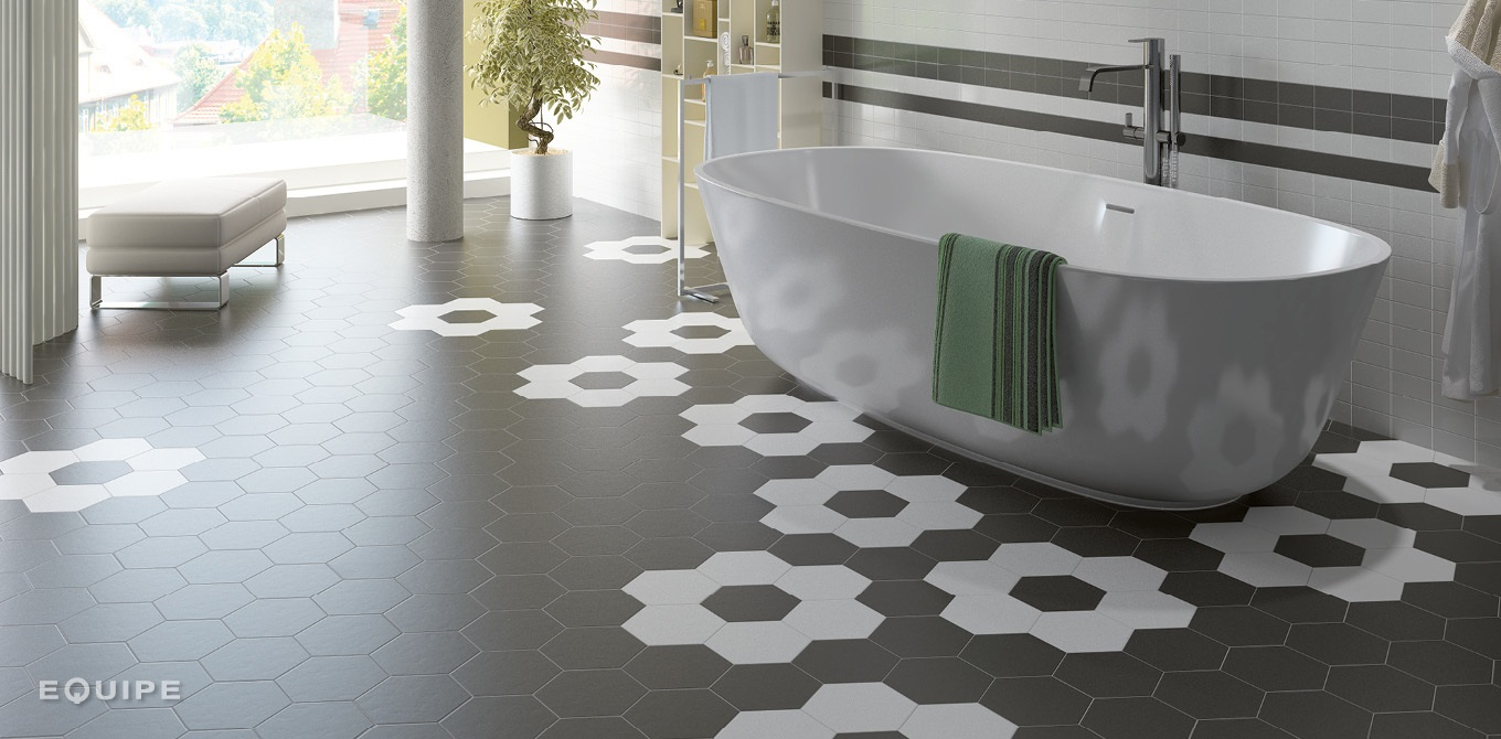 Carrelage hexagonal uni noir sur une salle de bain moderne blanche, avec baignoire, serviettes vertes, et mobilier épuré