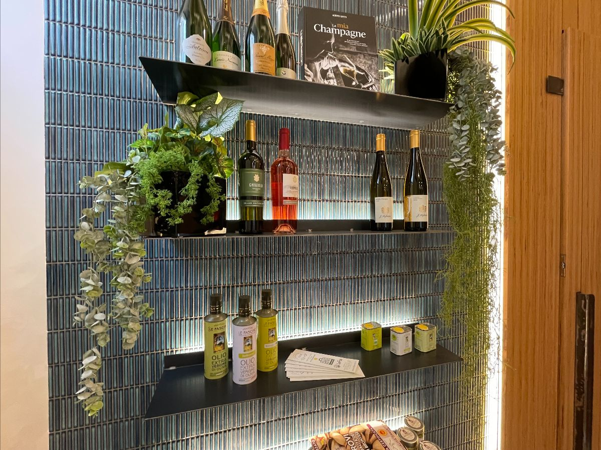 Carrelage uni bleu dans une cuisine moderne avec étagères, bouteilles de vin et plantes vertes sur fond boisé