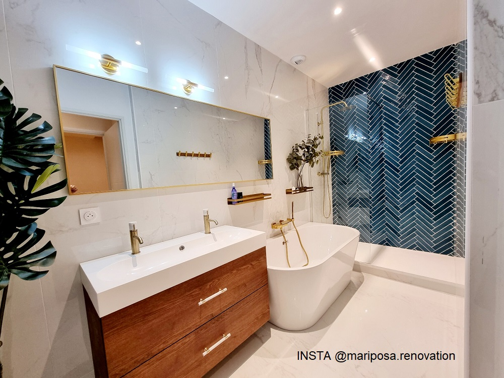 Carrelage Zellige bleu en chevron sur une salle de bain aux murs marbrés blancs avec baignoire et meuble en bois
