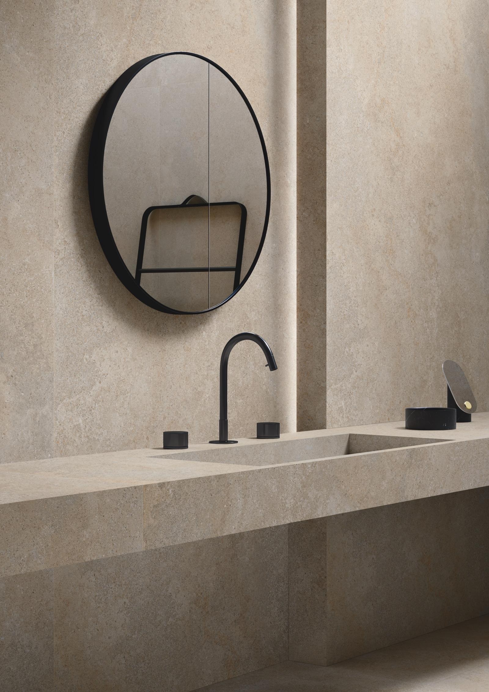 Carrelage effet pierre beige nuances claires et foncées 60x120 cm dans une salle de bain ton sur ton avec miroir rond et robinetterie noire