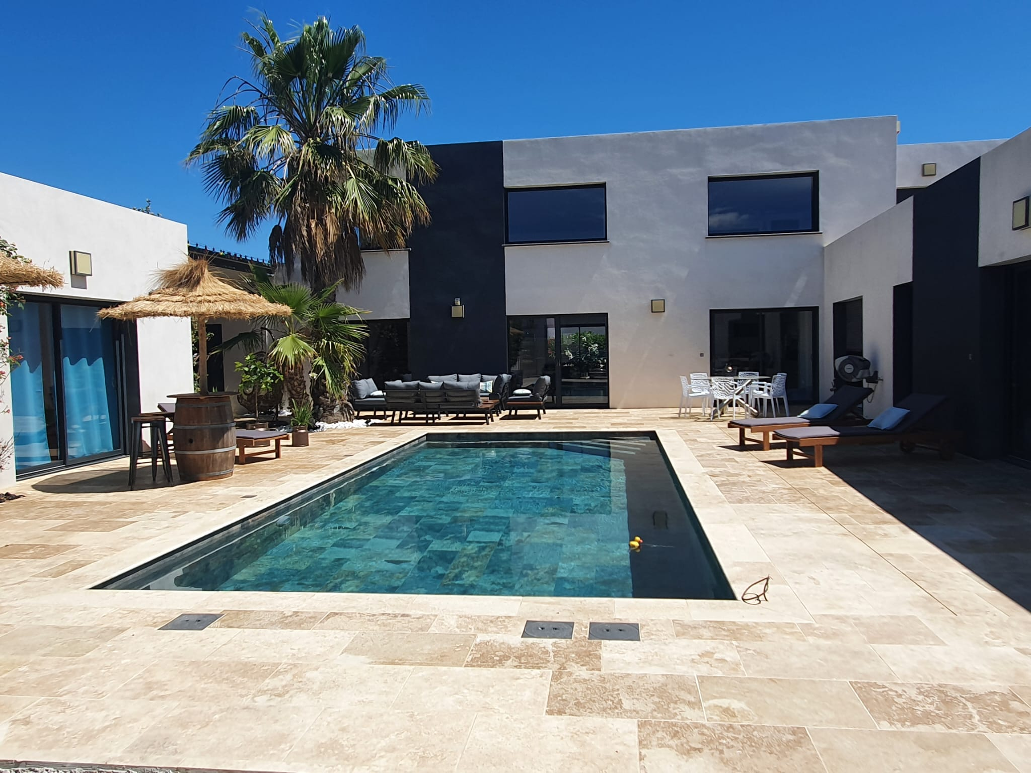 Carrelage aspect pierre terracotta dans un espace extérieur avec mobilier de jardin, palmiers et piscine sur fond de maison moderne grise